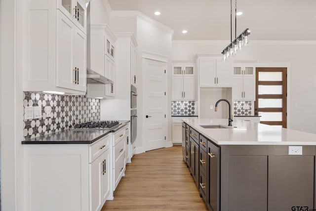 kitchen featuring stainless steel gas stovetop, hanging light fixtures, a kitchen island with sink, white cabinetry, and light hardwood / wood-style flooring