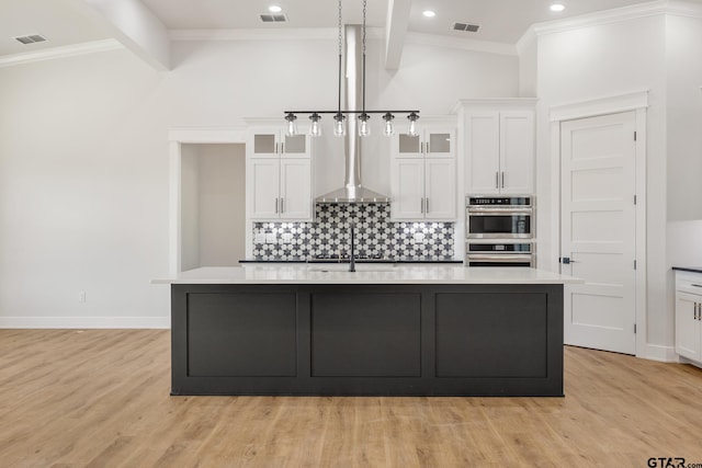 kitchen with light hardwood / wood-style floors, a kitchen island with sink, vaulted ceiling with beams, and tasteful backsplash