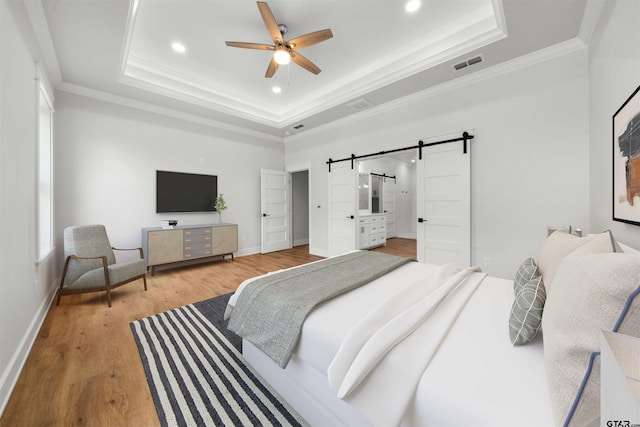 bedroom featuring wood-type flooring, a barn door, ceiling fan, and a tray ceiling