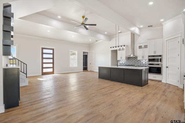 kitchen featuring white cabinetry, light hardwood / wood-style floors, wall chimney range hood, and an island with sink