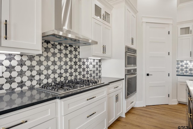 kitchen featuring tasteful backsplash, wall chimney range hood, white cabinetry, and stainless steel appliances