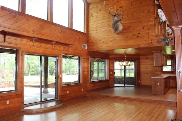 interior space with a notable chandelier, a high ceiling, light hardwood / wood-style flooring, and wood walls