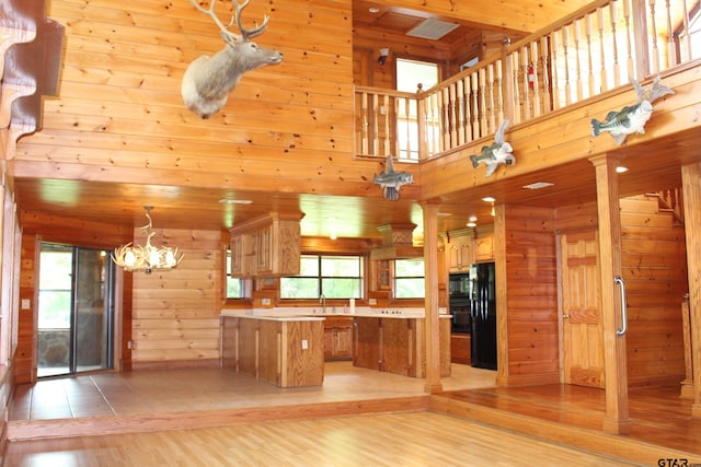 kitchen with black appliances, a center island, a healthy amount of sunlight, and wood walls