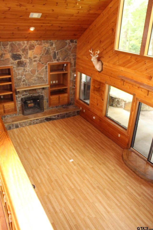 unfurnished living room featuring wood ceiling, wood-type flooring, a stone fireplace, and wood walls