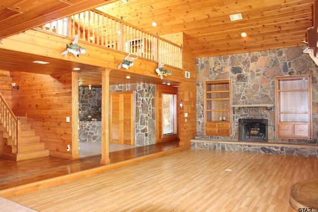 unfurnished living room with a stone fireplace, high vaulted ceiling, wood walls, wood-type flooring, and wooden ceiling