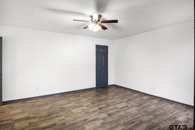 empty room with dark wood-type flooring, a ceiling fan, and baseboards