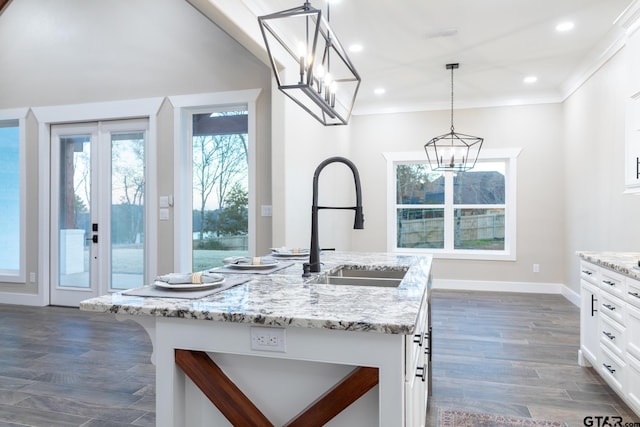 kitchen with dark hardwood / wood-style floors, decorative light fixtures, a kitchen island with sink, a notable chandelier, and white cabinets