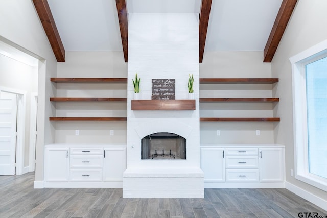 stairway with lofted ceiling with beams, wood-type flooring, built in desk, and a fireplace