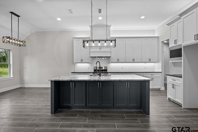 kitchen with pendant lighting, stainless steel microwave, a center island with sink, and light stone counters