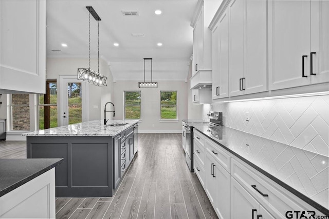 kitchen featuring a center island with sink, white cabinetry, appliances with stainless steel finishes, pendant lighting, and sink