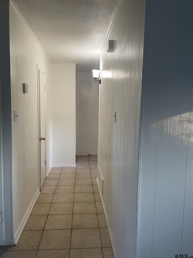 hall featuring ornamental molding, wooden walls, light tile patterned flooring, and a textured ceiling