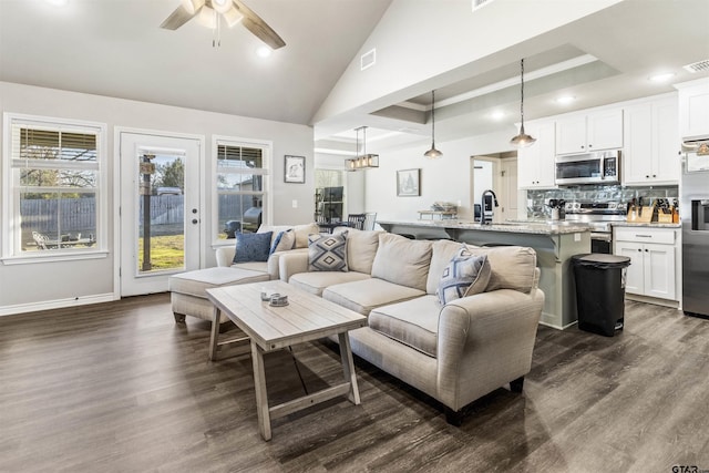 living room featuring ceiling fan, sink, dark hardwood / wood-style floors, vaulted ceiling, and a tray ceiling