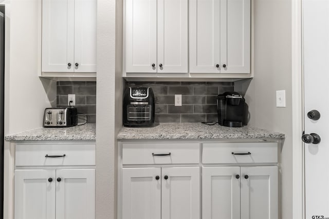 interior space with backsplash, light stone countertops, and white cabinets