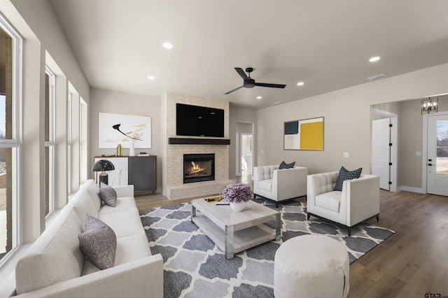 living room with a fireplace, ceiling fan with notable chandelier, and wood-type flooring