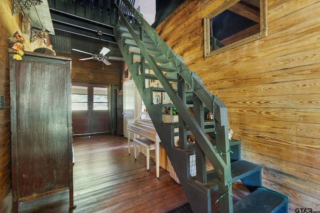 staircase with hardwood / wood-style floors, ceiling fan, and wooden walls