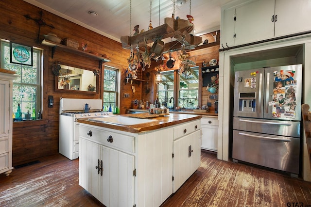 kitchen featuring a kitchen island, white range oven, stainless steel fridge, wood walls, and white cabinets