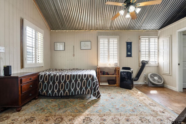 bedroom featuring ceiling fan, light hardwood / wood-style floors, lofted ceiling, and wooden walls