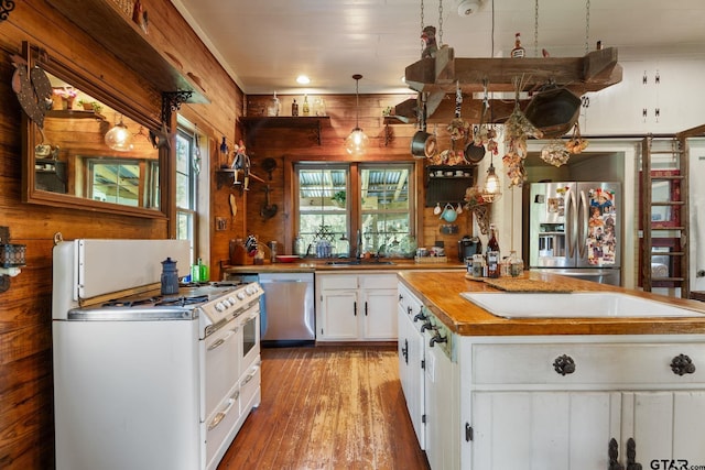 kitchen with light hardwood / wood-style flooring, wood walls, pendant lighting, white cabinets, and appliances with stainless steel finishes