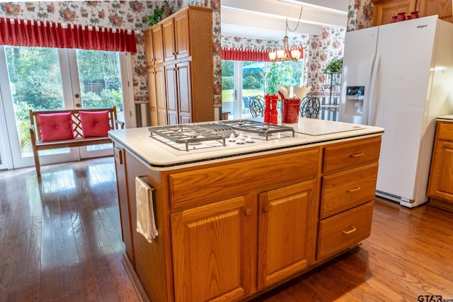 kitchen with a center island, hanging light fixtures, light wood-type flooring, a notable chandelier, and white appliances