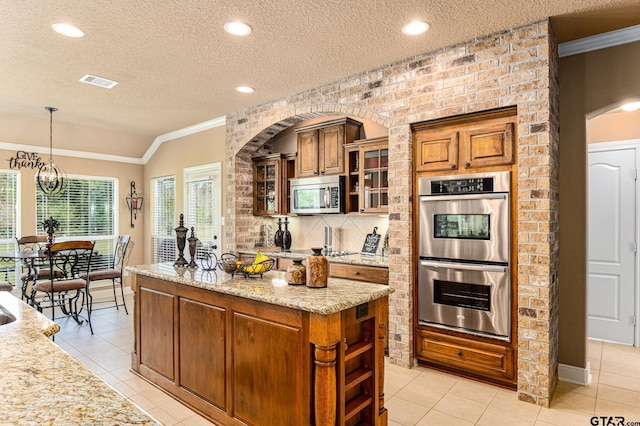 kitchen with stainless steel appliances, light stone counters, a textured ceiling, light tile patterned floors, and hanging light fixtures