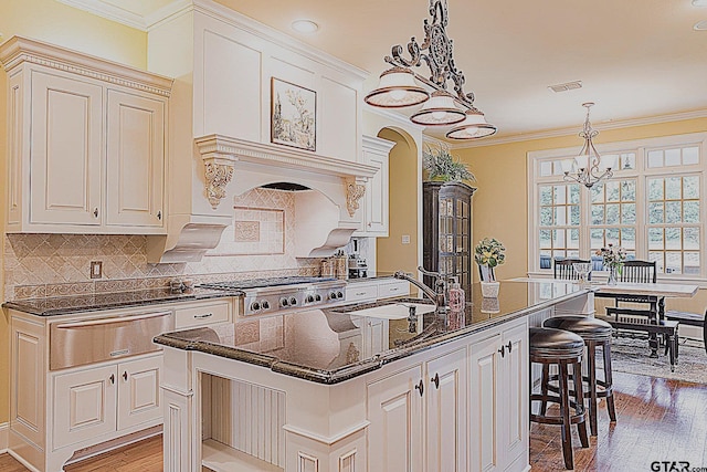 kitchen featuring sink, tasteful backsplash, pendant lighting, stainless steel gas stovetop, and a center island with sink