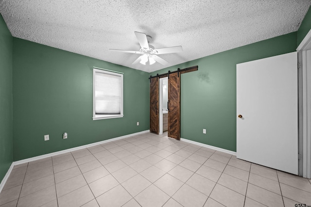 spare room featuring a barn door, ceiling fan, a textured ceiling, and light tile patterned floors