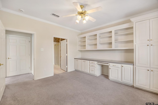 unfurnished office with ceiling fan, built in desk, light colored carpet, and ornamental molding