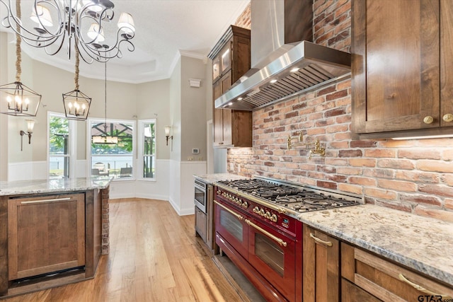 kitchen with light hardwood / wood-style floors, wall chimney exhaust hood, light stone counters, and ornamental molding