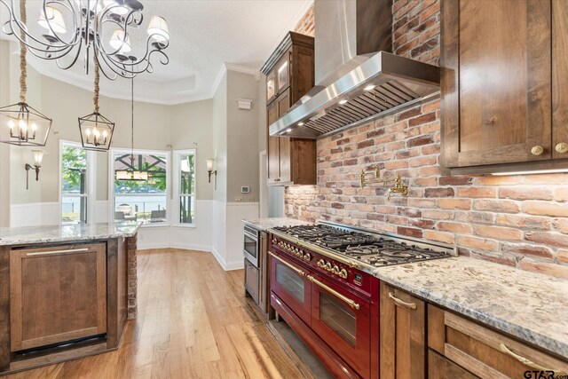 kitchen with light hardwood / wood-style floors, wall chimney exhaust hood, light stone counters, and ornamental molding