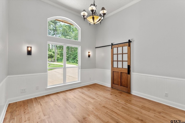 89 Eagle Cv, Mount Vernon, TX 75457 - spare room with a barn door, a wainscoted wall, a chandelier, light wood-type flooring, and crown molding