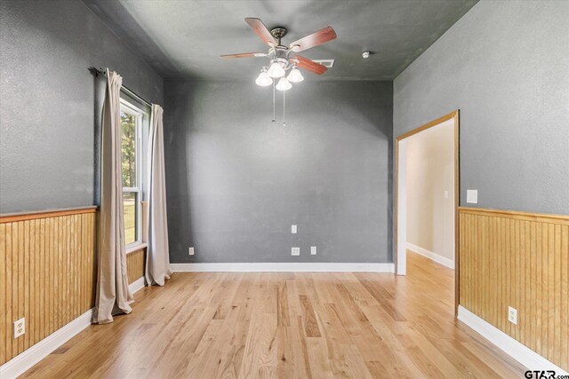 empty room with wood walls, light wood-type flooring, and ceiling fan