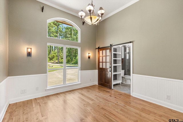 spare room featuring an inviting chandelier, a barn door, ornamental molding, light hardwood / wood-style flooring, and a high ceiling