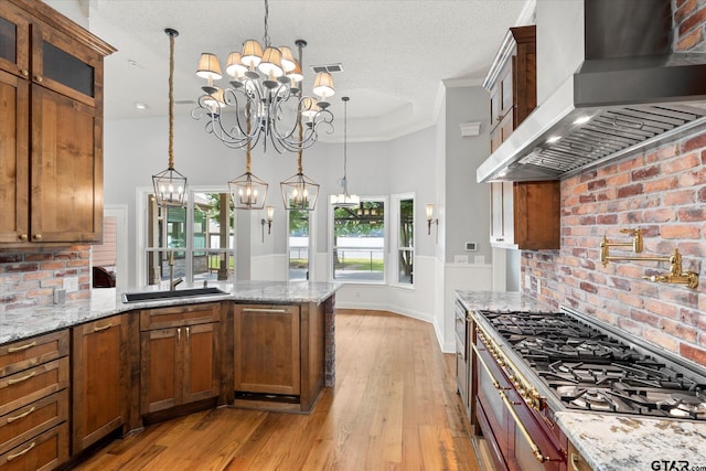 89 Eagle Cv, Mount Vernon, TX 75457 - kitchen featuring wall chimney exhaust hood, stainless steel gas stovetop, a chandelier, a peninsula, and brown cabinets
