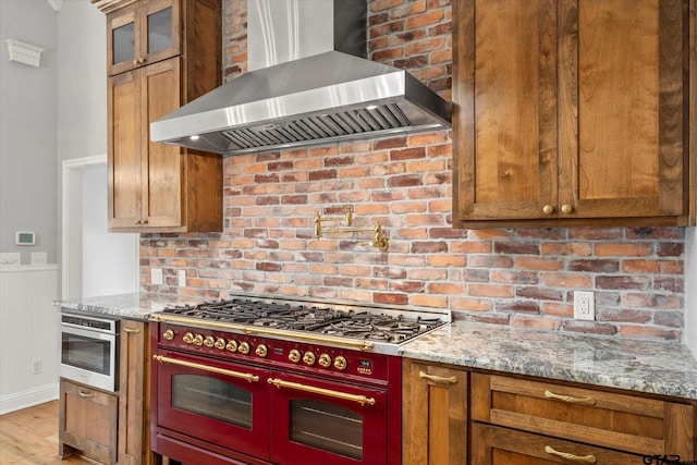 89 Eagle Cv, Mount Vernon, TX 75457 - kitchen with wall chimney range hood, double oven range, wainscoting, brown cabinets, and light stone counters