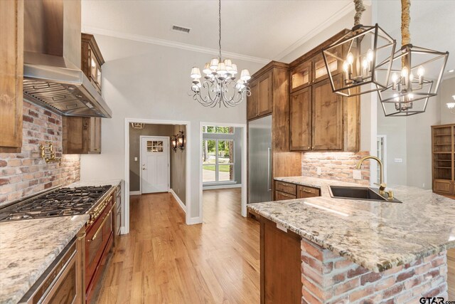 kitchen with sink, light stone counters, hanging light fixtures, wall chimney range hood, and light wood-type flooring