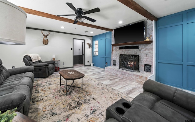 living room with ornamental molding, ceiling fan, beam ceiling, a fireplace, and light wood-type flooring