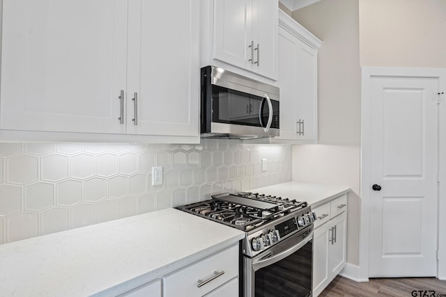 kitchen with appliances with stainless steel finishes, white cabinetry, light hardwood / wood-style floors, backsplash, and light stone counters