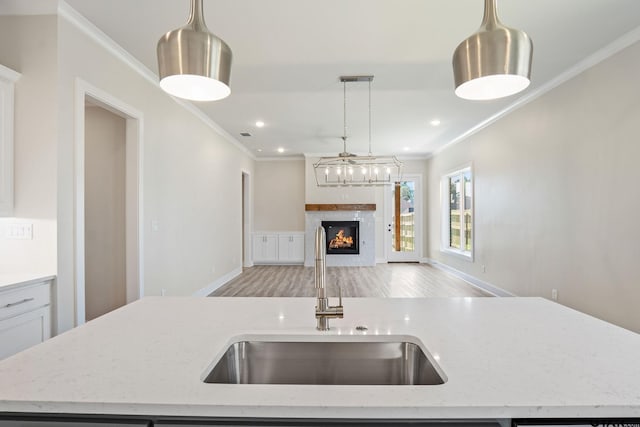 kitchen featuring sink, decorative light fixtures, a center island with sink, and light stone countertops