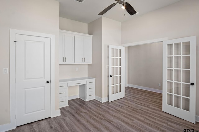 unfurnished office featuring wood-type flooring, ceiling fan, built in desk, and french doors