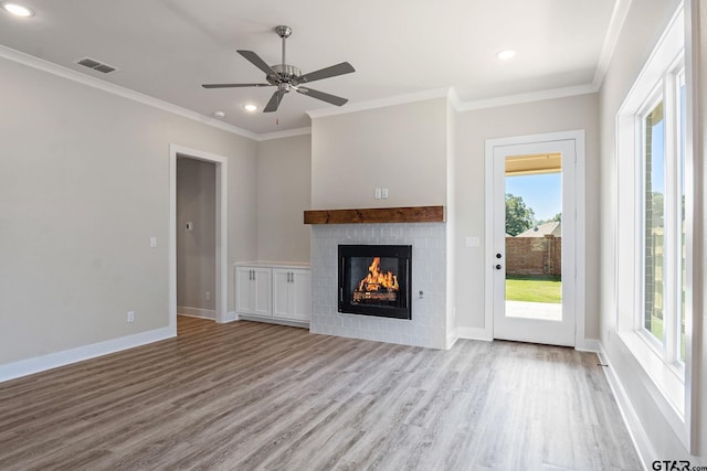 unfurnished living room featuring a brick fireplace, light wood-type flooring, ornamental molding, and a healthy amount of sunlight