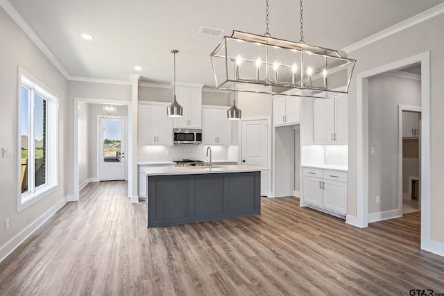 kitchen featuring hanging light fixtures, white cabinets, a center island with sink, and crown molding