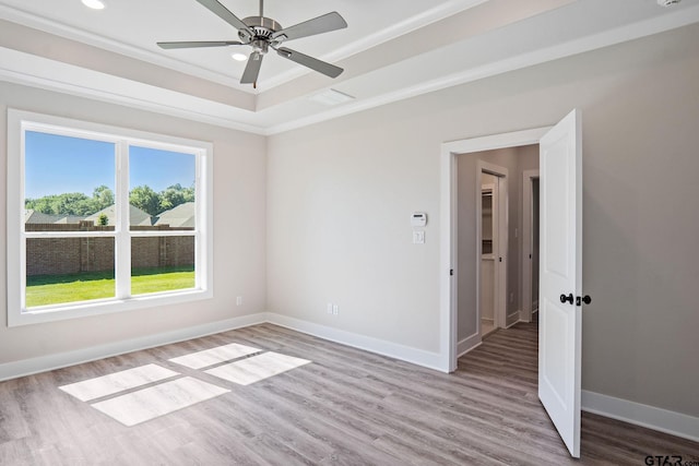 unfurnished room featuring light wood-type flooring, ceiling fan, a raised ceiling, and crown molding