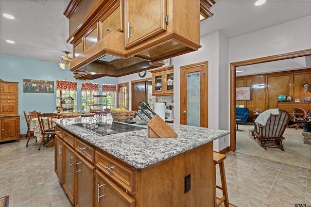 kitchen with a kitchen bar, light colored carpet, black electric cooktop, a center island, and ceiling fan