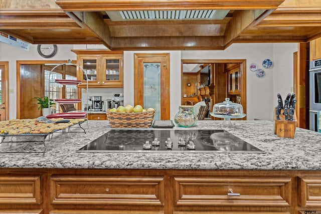 kitchen featuring stainless steel oven, light stone countertops, black electric stovetop, and beam ceiling