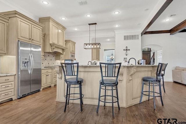 kitchen with light stone countertops, stainless steel fridge, an island with sink, and hanging light fixtures