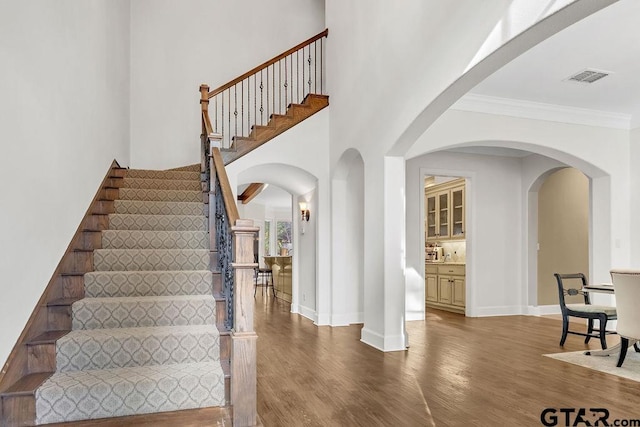 stairs featuring hardwood / wood-style floors, a high ceiling, and ornamental molding