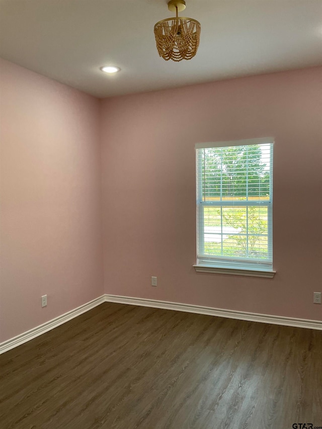 empty room with dark hardwood / wood-style flooring and an inviting chandelier