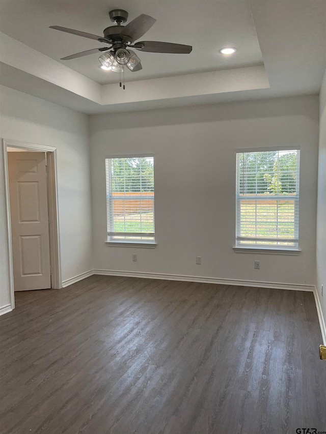 unfurnished room with dark wood-type flooring, a healthy amount of sunlight, a raised ceiling, and ceiling fan