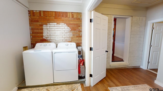 laundry room featuring light wood-type flooring, brick wall, and washing machine and clothes dryer