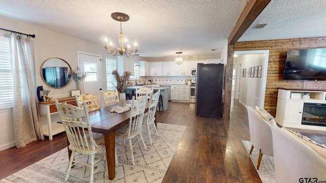 dining area with wood walls, light hardwood / wood-style floors, sink, a textured ceiling, and a notable chandelier